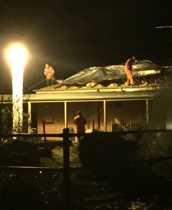 HARD WORK: Leeton SES volunteers work to cover the gaping hole in the Gready family's roof after it was blown off. 