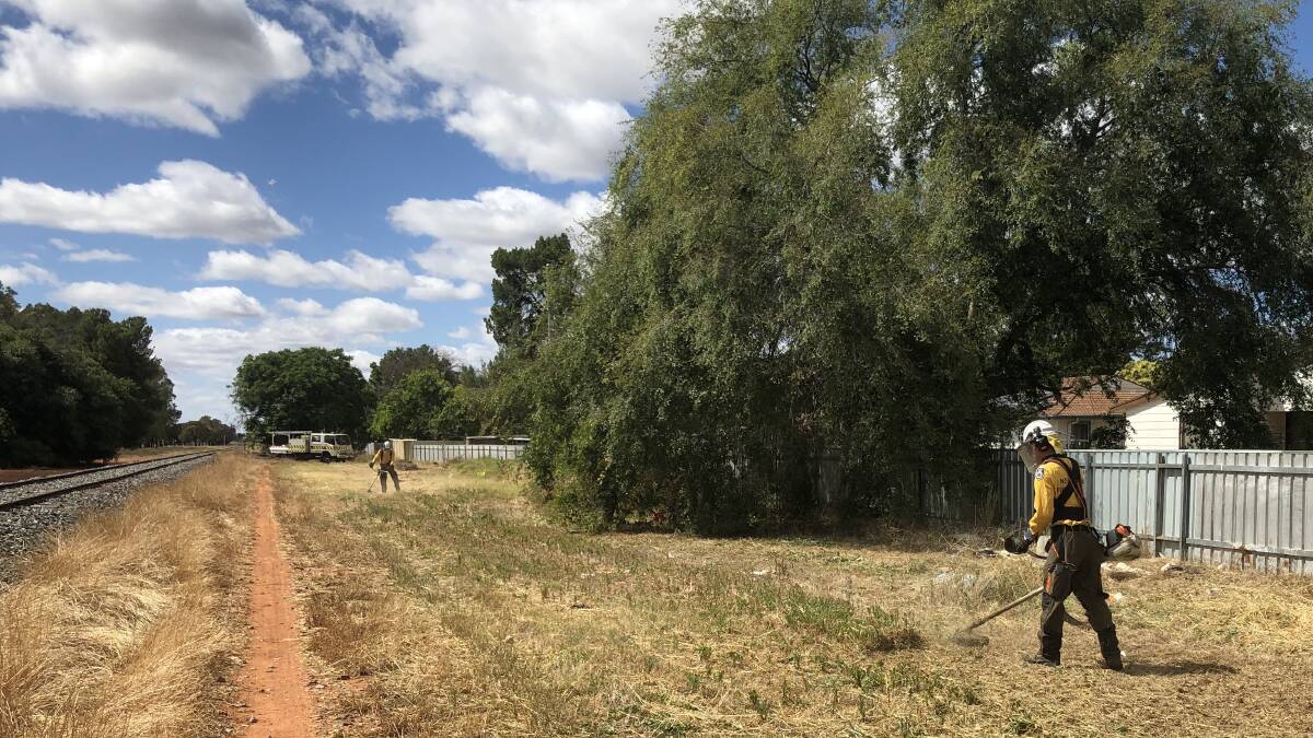 Members of the State Mitigation Support Services remove grass growth from around homes on Parkinson Crescent. PHOTO: Monty Jacka